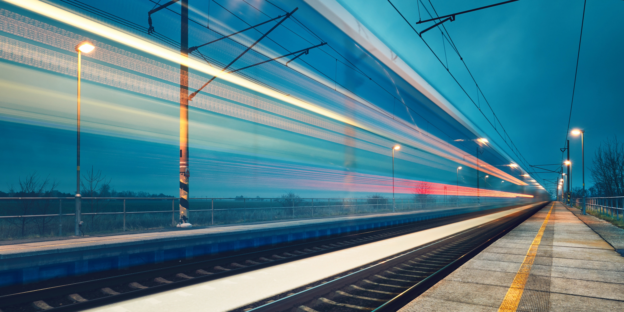 Schnell fahrender Zug auf einem leeren Bahnsteig bei Nacht, dargestellt als Lichtstreifen aufgrund der Geschwindigkeit.